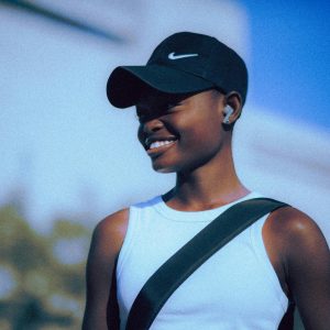 Portrait of a smiling woman wearing a cap and wireless headset outdoors in summer.